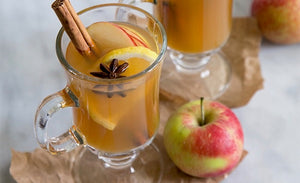 Clear glass mug of apple cider cocktail with cinnamon stick, five star anise, lemon and apple garnish