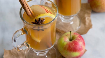 Clear glass mug of apple cider cocktail with cinnamon stick, five star anise, lemon and apple garnish
